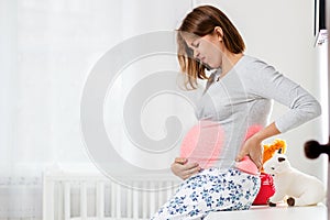 A young pregnant woman is experiencing lower back and abdominal pain. Children`s room in the background. The concept of pregnant