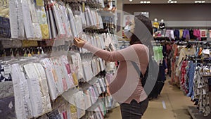 Young pregnant woman with glasses and a medical mask in a baby store. The girl chooses clothes for the unborn child.