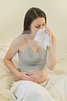 Young pregnant woman with handkerchief sitting in bed at home