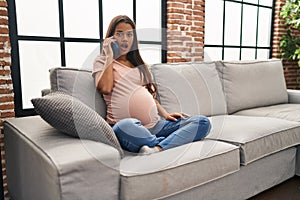 Young pregnant woman having conversation speaking on the smartphone scared and amazed with open mouth for surprise, disbelief face