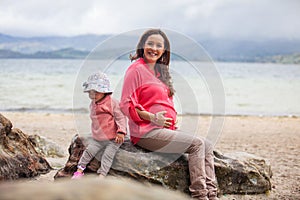 Young pregnant woman having fun with her baby girl at the beautiful white beach of Lake Tota located in the department of Boyaca