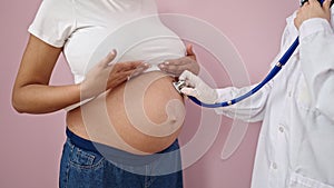 Young pregnant woman having medical examination with stethoscope over isolated pink background