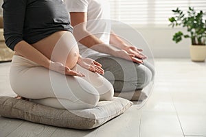 Young pregnant woman with her husband practicing yoga at home, closeup