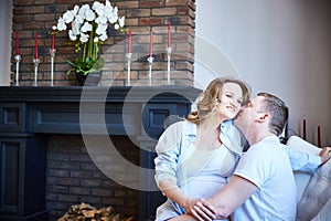 young pregnant woman and her husband are sitting in a chair in their house. Lifestyle.