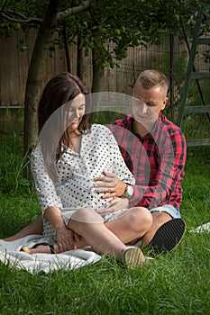 Young pregnant woman and her husband sitting in the garden