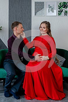 Young pregnant woman with her husband sitting on the sofa in studio