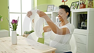 Young pregnant woman holding pyjama sitting on table at dinning room