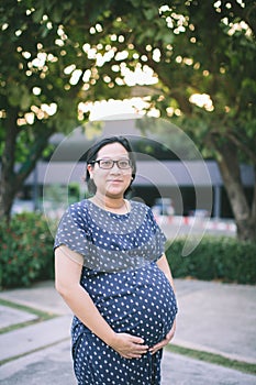 Young pregnant woman holds her hands on her swollen belly.