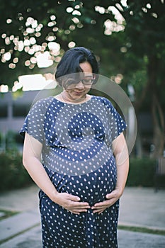 Young pregnant woman holds her hands on her swollen belly.