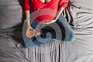 young pregnant woman at home holding a cup of decaffeinated coffee