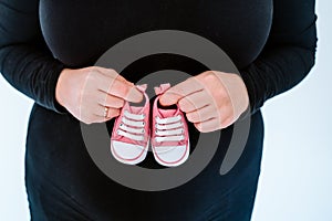 young pregnant woman home holding tiny pink baby shoes. family concept. close up