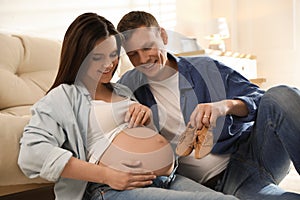 Young pregnant woman and husband with baby`s shoes at home