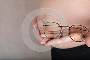 Young pregnant woman keeps eye glasses in front of her belly