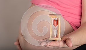 Young pregnant woman keeps sandwatch close to her belly