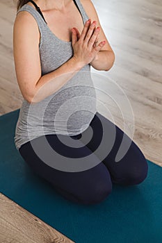 Young pregnant woman kneeling on a yoga mat meditating