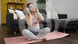Young pregnant woman listening to music sitting on yoga mat at home
