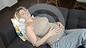 Young pregnant woman listening to music touching belly sleeping on sofa at home