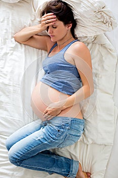 Young pregnant woman lying in bed with pain