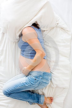 Young pregnant woman lying in bed with pain