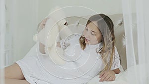 A young pregnant woman lying on the bed and playing with soft toy.