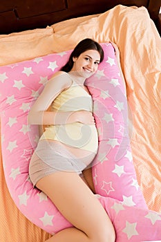 Young pregnant woman lying in bed with supportive pillow