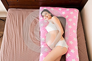 Young pregnant woman lying in bed with supportive pillow