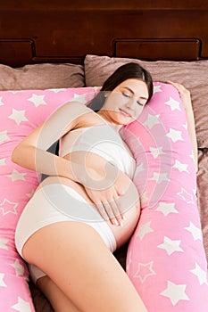 Young pregnant woman lying in bed with supportive pillow