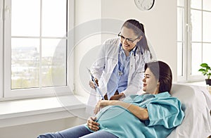 Young pregnant woman lying on the couch visiting gynecologist doctor in hospital or medical clinic.