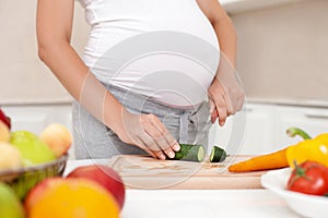 Young pregnant woman is making a salad in kitchen