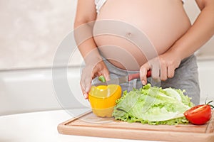 Young pregnant woman is making a salad in kitchen