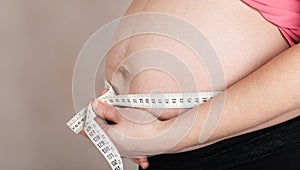 Young pregnant woman measures her belly with measurement band