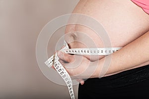 Young pregnant woman measures her belly with measurement band