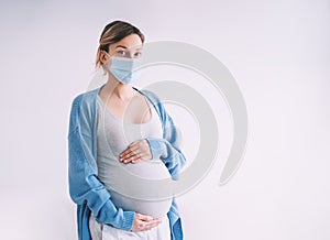 Young pregnant woman in medical mask hugging belly. Pregnancy and childbirth during infectious diseases