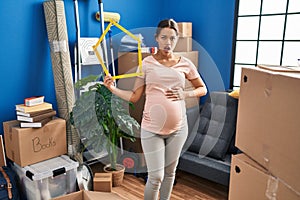Young pregnant woman moving to a new home in shock face, looking skeptical and sarcastic, surprised with open mouth