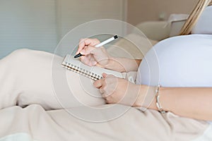 Young Pregnant woman packing suitcase for maternity hospital at home, closeup. Checklist for childbirth. Pregnancy during