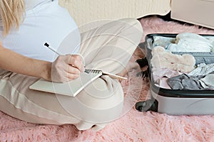 Young Pregnant woman packing suitcase for maternity hospital at home, closeup. Checklist for childbirth. Pregnancy during