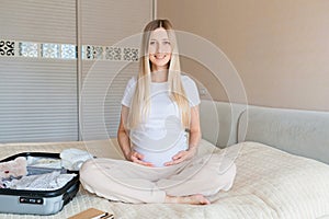 Young Pregnant woman packing suitcase for maternity hospital at home, closeup. Checklist for childbirth. Pregnancy