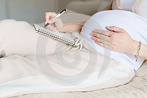 Young Pregnant woman packing suitcase for maternity hospital at home, closeup. Checklist for childbirth. Pregnancy