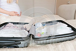 Young Pregnant woman packing suitcase for maternity hospital at home, closeup. Checklist for childbirth. Pregnancy