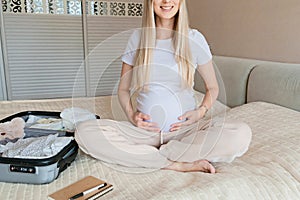 Young Pregnant woman packing suitcase for maternity hospital at home, closeup. Checklist for childbirth. Pregnancy