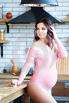 Young pregnant woman in pink bodysuit drinking water in the kitchen. How to get rid of morning sickness and toxemia. Drugs and
