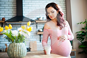 Young pregnant woman in pink bodysuit drinking water in the kitchen. How to get rid of morning sickness and toxemia. Drugs and