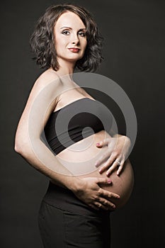 Young pregnant woman posing on black background.