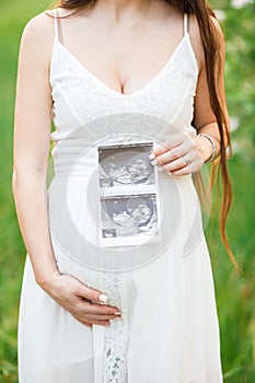 Young, pregnant woman posing in a white negligee dress