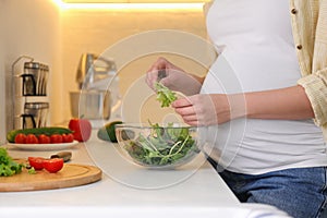 Young pregnant woman preparing vegetable salad at table in kitchen, closeup. Healthy eating