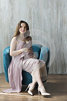 A young pregnant woman in a purple dress sitting on a chair.