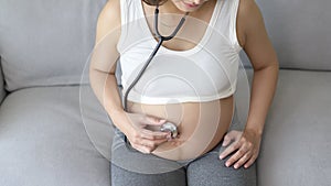 Young pregnant woman putting stethoscope on tummy, healthcare and pregnancy care concept