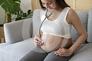 Young pregnant woman putting stethoscope on tummy, healthcare and pregnancy care concept