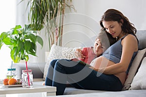 Young pregnant woman, reading a book at home to her boy