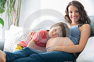 Young pregnant woman, reading a book at home to her boy